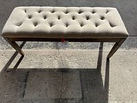 Front angled view of the tufted beige fabric bench showing the tufting detail and wooden legs.