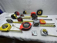 Wide view of all measuring tapes laid on white cloth showing various sizes and brands.