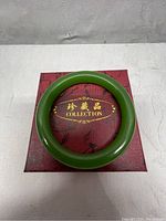 Top-down view of green jade bangle resting on red collection box