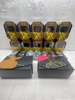 Front view of ten empty Pokémon trading card metal tins with Pikachu window display and two rectangular Crown Zenith Pokémon TCG themed boxes in front.