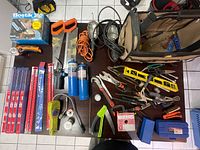 Photo showing a spread of various tools on a floor including saws, cans, and hand tools along with a large brown tool bag.