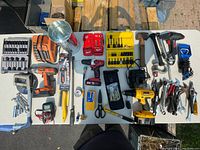Wide view of all tools in the lot showing drills, charger, hammer, pliers, scissors, measuring tape, and various bits and accessories.