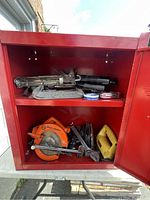 Red metal cabinet with open doors showing various power tools and hand tools on two shelves.