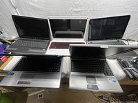 Photo showing six assorted used laptops open and arranged on a surface, showing keyboards and screens from a top angle.