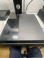 Front and top view of black Sony PlayStation 4 console showing some wear and fingerprints.