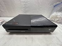 Top front angle view of the Xbox One console showing Xbox logo and disc slot on front, vented half on top.