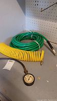 Two air hoses, yellow coiled and green coiled, placed on grey surface near pegboard. One hose has a gauge attached.