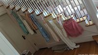 Seven vintage aprons hanging from a staircase railing, various styles and colors visible including red checkered, blue floral, plain white.