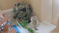 Photo showing two glass frog figurines, two small glass bug figurines, and large art glass plate with abstract design mounted on metal stand.