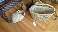Overview photo showing all baskets including large rectangular basket with handle and several round baskets with and without lids on wooden floor.