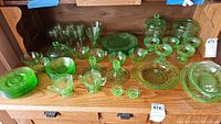 Overall group shot of green uranium glass pieces on wood furniture