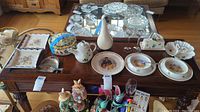 Overview of the lot items on a wooden table including Royal Baby plates, ceramic duck, crumb sweeper, teapot, and other ceramic items.