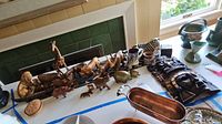 Wide shot showing carved wood animal figurines including giraffe and lion, ceramic zebra mugs, large carved wood mask, and brass trinket boxes on table