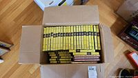 Open cardboard box showing multiple yellow-spined Nancy Drew hardcover books arranged in two layers inside.