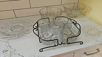 Glass serving ware items arranged on a white marble countertop, including a divided relish dish in metal holder, large bowls, and smaller dishes.