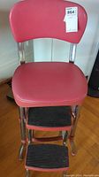 Full view of the red vinyl and chrome metal framed step stool with two rubber tread steps.