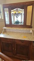 Full view of the vintage wooden vanity cabinet with marble countertop and attached large mirror. Shows overall structure and condition.