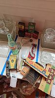 Overview of five tins, Coca-Cola bottle, Crayola crayons, fish scaler, and assorted kitchen utensils in a box