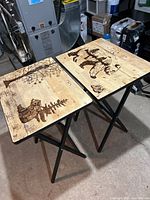 Two wooden TV tables with bear art on tops, standing on black folding legs in a basement setting.