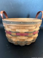 Exterior close-up showing woven pattern with red and dark brown strips and leather handles.