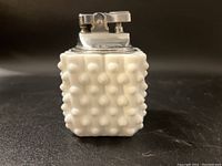 Front view of white milk glass hobnail patterned table lighter with metal ignition piece on top against dark background.
