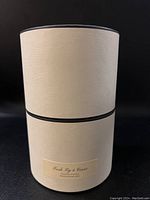 Cylindrical cream-colored textured box with a black trim, label reads 'Fresh Fig & Cassis Scented Candle Bougie Parfumée'.