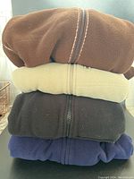 Stack of four folded fleece hoodies in brown, beige, black, navy blue colors, showing their texture and zip line details.