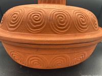Close-up of roaster side showing embossed spiral pattern on terracotta clay.