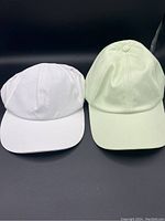 Two Lululemon hats side by side, one white and one light green, shown from the front.