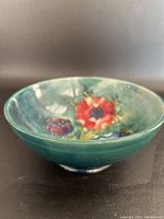 Side angled view of Moorcroft bowl showing raised colorful flower motifs and green interior glaze.