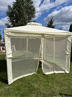 Full front view of cream colored Outsunny gazebo set up outdoors on grass. Shows mesh screened walls with zippered door openings. Soft top roof with vented peak seen.