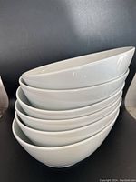 Stack of six identical white porcelain serving bowls showing their shape and finish.