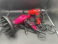 Two hair dryers together showing power cords and attachments, black background