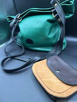 Green and black leather tote bag with black straps and smaller brown and tan leather carry bag in front of it.