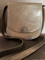 Front view of the dark green leather messenger bag with flap and strap on a dark background.