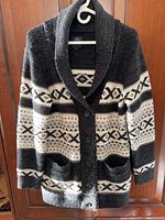 Full front view of the black, white, and gray patterned knit sweater coat hanging on a wooden door.