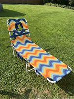Full length view of tanning chair on grass showing colorful wavy fabric design and metal frame.