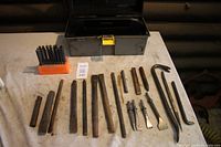 Full lot shot showing air chisel bits set in holder, multiple chisels, wrecking bars, punches, and black toolbox.