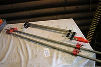 Four bar clamps laid out on a white cloth surface with two shorter clamps (24-inch) and two longer clamps (55-inch) visible.