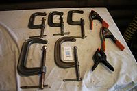 Set of five metal C-clamps and three plastic spring clamps arranged on table surface