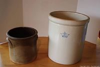 Image capturing both crocks side by side on wooden surface showing size difference and overall condition.