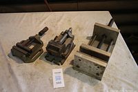 Three drill press vises placed on a table showing full front view of all vises in the lot.