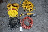 Full lot top-down outdoor view showing yellow extension cord on caddy, loose yellow extension cord, black and orange corded trouble lights, orange extension cord, and a ground fault interrupter link.