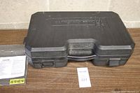 Closed black hard plastic carrying case with Michelin logo embossed on lid, set on wooden surface alongside paperwork and auction card.