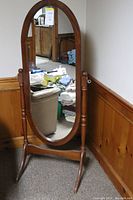 Full view of the oval free standing swinging mirror with wooden frame in a room corner. Shows its proportions and design.