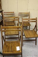 View of all five dark stained wooden folding chairs, arranged with four in the back and one front right folded open.