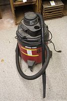 Front view of red Shop-Vac 8 gallon unit with black hose and nozzle attached, showing brand name and capacity.
