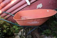 Full side view of orange wheelbarrow showing Erie WM60 Landscaper branding, black metal handles and frame, and single black rubber wheel.