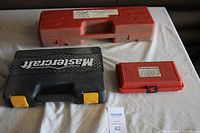 Three tool cases on a table: red case (dent puller set), red plastic case (Noid Lite set), black Mastercraft case (socket set).