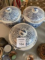 Three white porcelain jars with lids, decorated in blue geometric and floral patterns on a table surrounded by other decorative items.